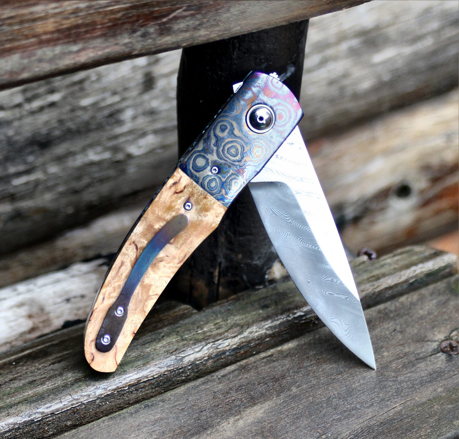 A finished liner-lock folding knife with mokume bolster and burl handle, blade open